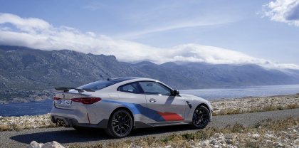 Seitenansicht BMW M4 Coupé auf einer Straße, mit Bergen und See im Hintergrund.